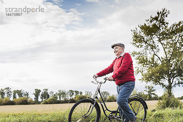 Älterer Mann schiebt Fahrrad in ländlicher Landschaft