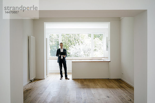 Immobilienmakler wartet in frisch renoviertem Haus  mit Laptop in der Hand