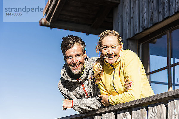 Lächelndes  auf dem Balkon einer Berghütte lehnendes Paar