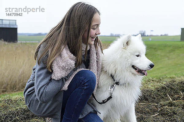Lächelndes Mädchen  das neben seinem Hund auf einer Wiese kauert