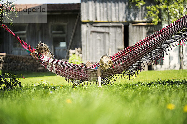 Zwei Kinder entspannen sich in der Hängematte im Garten eines Bauernhofs