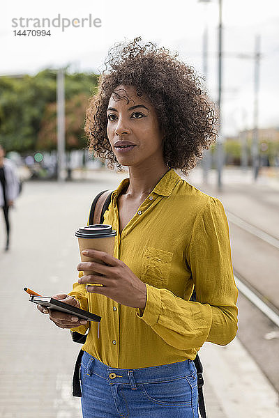 Porträt einer Frau mit Kaffee zum Mitnehmen und Notizbuch in der Stadt