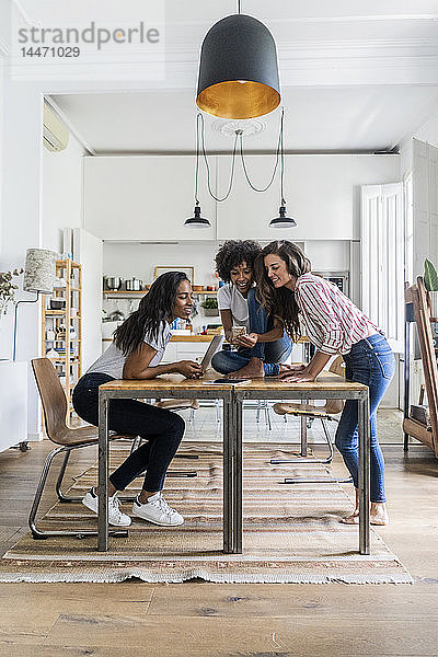 Drei glückliche Frauen mit digitalen Geräten auf dem Tisch zu Hause