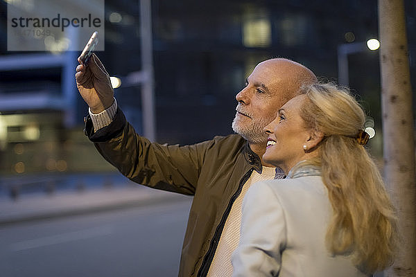 Spanien  Barcelona  glückliches älteres Ehepaar  das in der Abenddämmerung ein Selfie in der Stadt macht