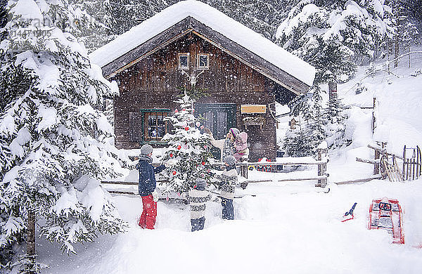 Österreich  Altenmarkt-Zauchensee  Familie schmückt Weihnachtsbaum am Holzhaus