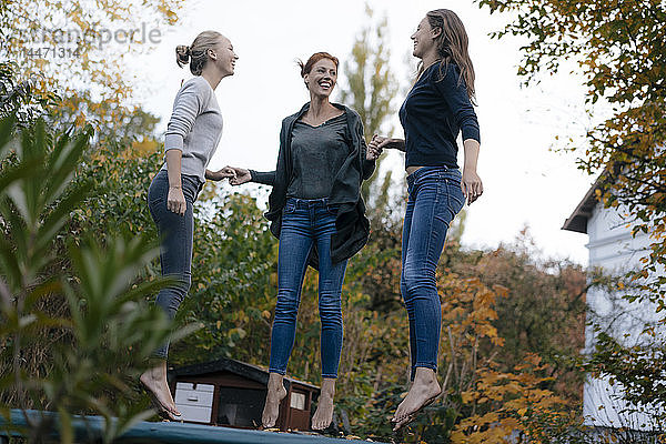 Glückliche Mutter mit zwei Mädchen im Teenageralter  die im Herbst im Garten auf dem Trampolin springen