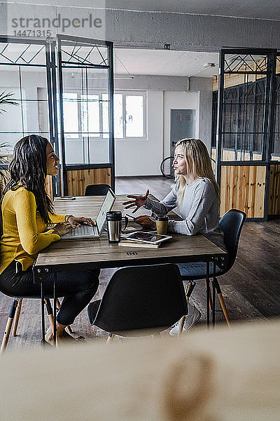 Zwei junge Geschäftsfrauen unterhalten sich am Konferenztisch im Loft-Büro