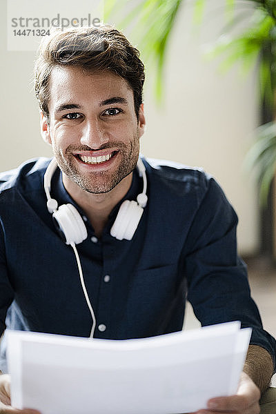 Porträt eines lächelnden jungen Mannes mit Kopfhörern  der Papiere hält