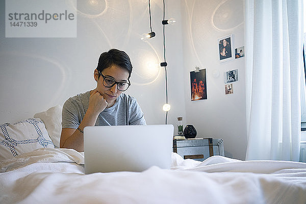 Junge Frau sitzt im Bett und benutzt einen Laptop