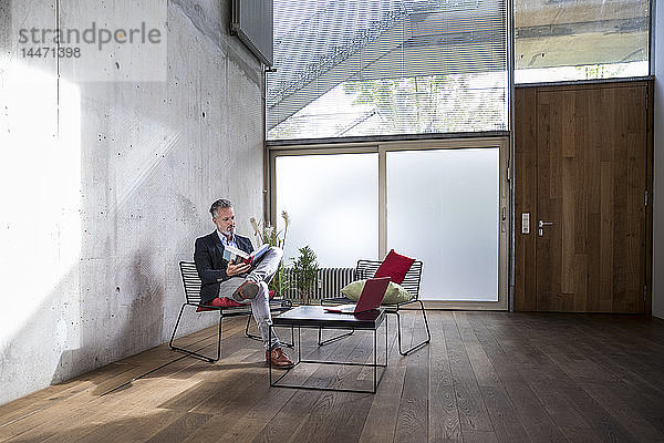 Geschäftsmann sitzt auf einem Dachboden an Betonwand und liest Buch