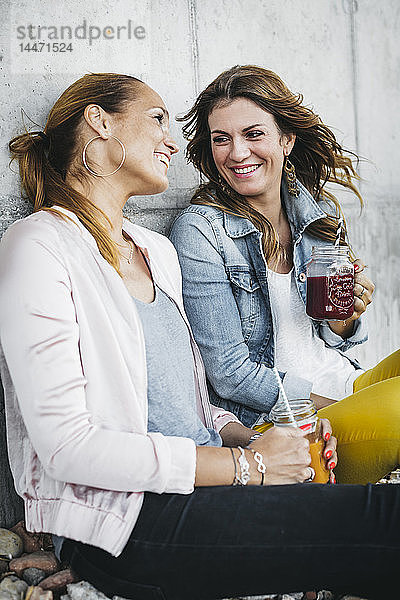 Zwei Freundinnen trinken Smoothies im Freien und amüsieren sich