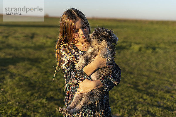 Porträt eines zufriedenen Mädchens mit Hund auf dem Arm bei Sonnenuntergang