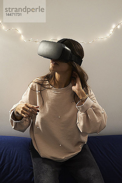 Junge Frau mit VR-Headsets spielt nachts zu Hause auf dem Sofa Spiele