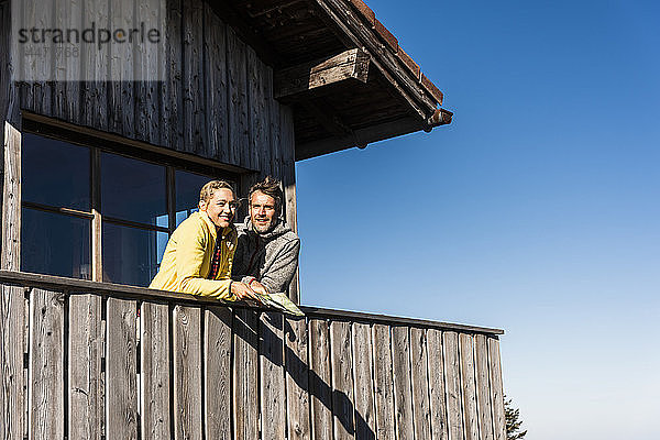 Paar lehnt auf dem Balkon einer Berghütte  hält Karte