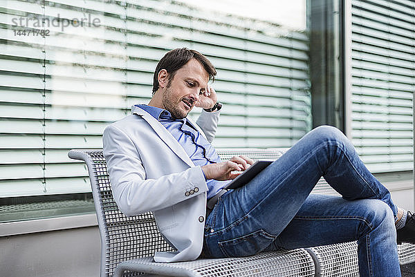 Geschäftsmann sitzt auf einer Bank und verwendet ein digitales Tablett