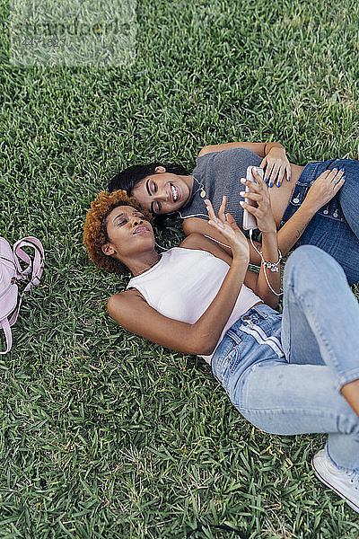 Zwei Freundinnen entspannen sich in einem Park und hören Musik