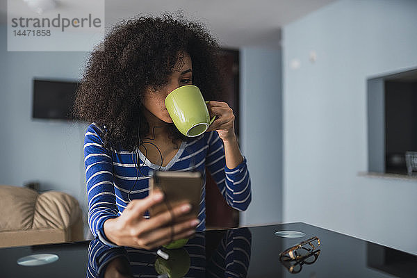 Junge Frau trinkt Kaffee  während sie auf ihr Handy schaut