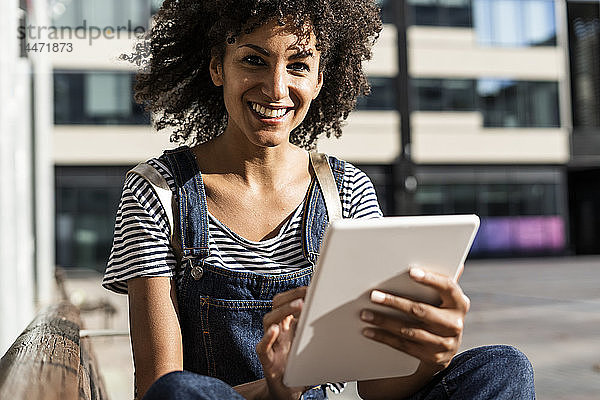 Mittlere erwachsene Frau mit lockigem Haar  die auf einer Bank sitzt und ein digitales Tablett benutzt