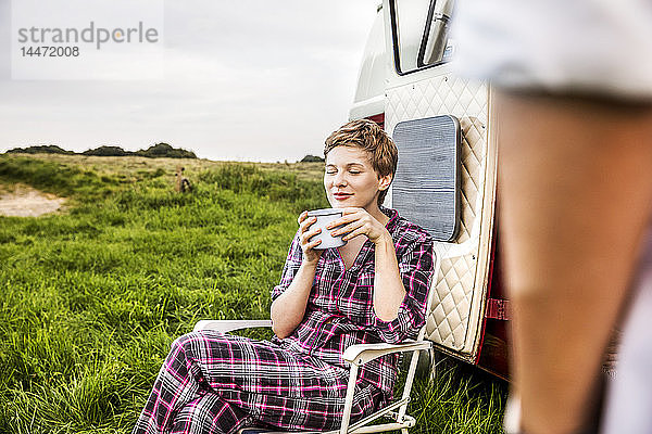 Frau im Pyjama genießt Kaffee in einem Lieferwagen auf dem Land