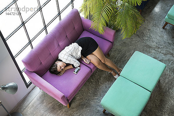 Draufsicht einer müden Geschäftsfrau  die im Büro auf einer violetten Couch schläft