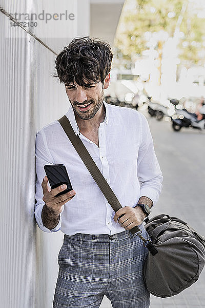 Junger Mann mit Tasche telefoniert mit seinem Handy in der Stadt