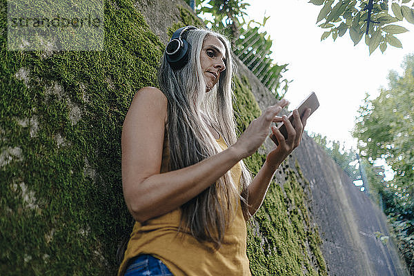 Frau mit Handy steht im Garten und hört Musik mit Kopfhörern