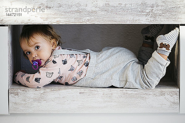 Porträt eines kleinen Mädchens mit Schnuller  das sich zu Hause versteckt