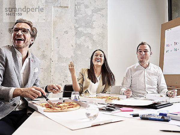Lachende Kollegen machen Mittagspause mit Pizza im Konferenzraum