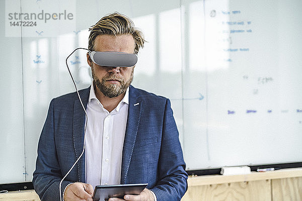 Geschäftsmann im Büro stehend  mit VR-Brille und digitalem Tablet