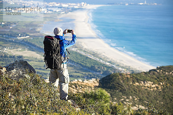 Spanien  Andalusien  Tarifa  Mann auf einer Wanderung an der Küste beim Fotografieren mit dem Handy