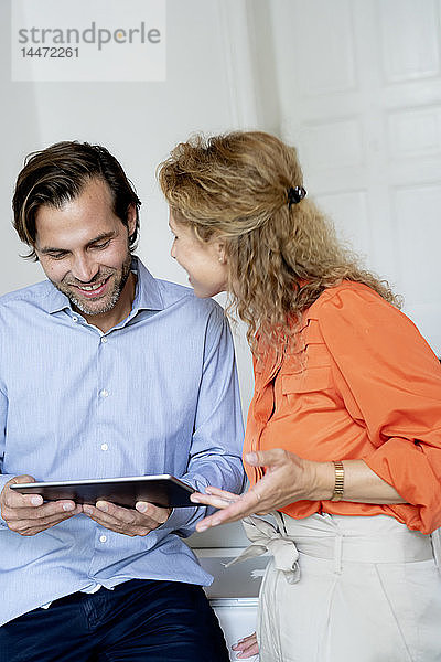 Glückliches Paar arbeitet von zu Hause aus und diskutiert über ein digitales Tablet