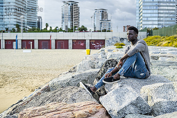 Junger Mann sitzt auf Felsen am Strand und entspannt sich