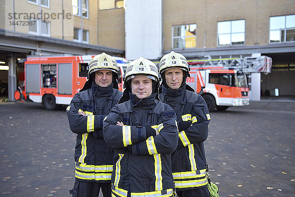 Porträt von drei selbstbewussten Feuerwehrleuten  die auf dem Hof vor dem Löschfahrzeug stehen