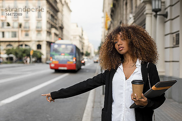 Junge Frau mit Laptoptasche und Kaffee zum Mitnehmen in der Stadt  ein Taxi rufend