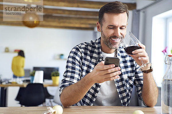 Mann sitzt am Tisch  benutzt Smartphone  entspannt sich bei einem Glas Rotwein