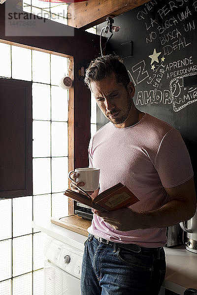 Mann mit Tasse Kaffee liest ein Buch in der Küche