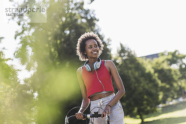 Lächelnde sportliche junge Frau mit Fahrrad im Park