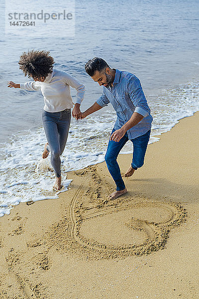 Spanien  Barcelona  glückliches Paar am Strand  das sich am Strand vergnügt und ein Herz in den Sand zeichnet