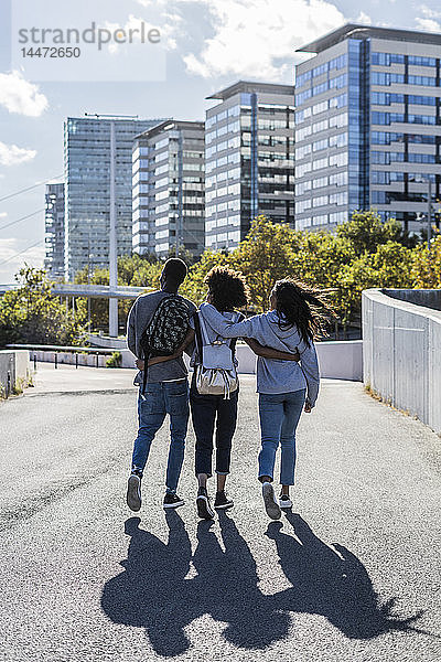 Drei Freunde erkunden die Stadt  gehen Arm in Arm die Straße entlang