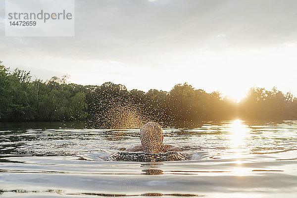 Älterer Mann schwimmt bei Sonnenuntergang in einem See