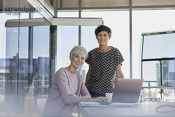 Porträt von zwei lächelnden Geschäftsfrauen mit Laptop am Schreibtisch im Büro