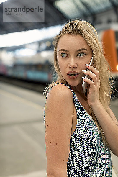 Porträt einer jungen Frau am Bahnhof  die sich am Handy umsieht
