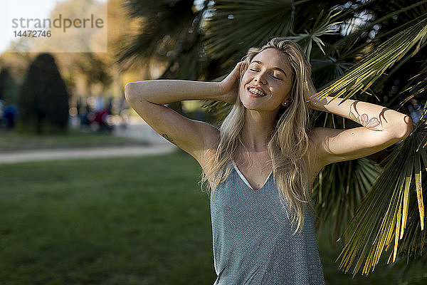 Porträt einer glücklichen jungen Frau an einer Palme im Park