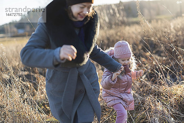 Kleines Mädchen rennt Hand in Hand mit ihrer Mutter zur goldenen Stunde auf der Herbstwiese