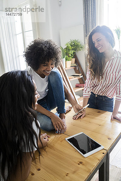 Drei glückliche Frauen schauen auf Handy auf dem Tisch zu Hause