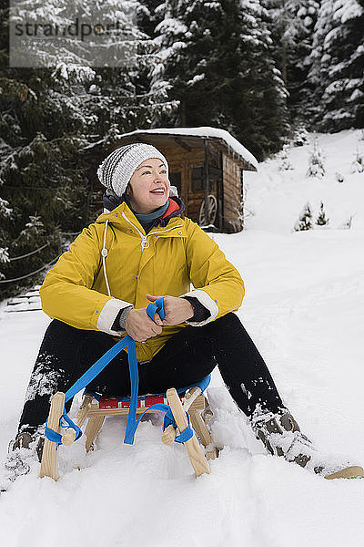 Österreich  Tirol  Thurn  zufriedene reife Frau sitzt auf Schlitten im Schnee und schaut in die Ferne