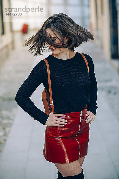 Lächelnde junge Frau in rotem Lacklederrock mit Reißverschluss  die ihr Haar wirft