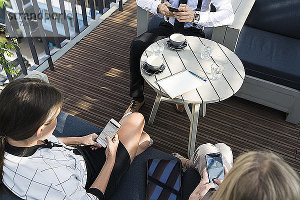 Drei Geschäftskollegen machen eine Kaffeepause auf der Stadtterrasse und überprüfen Smartphones