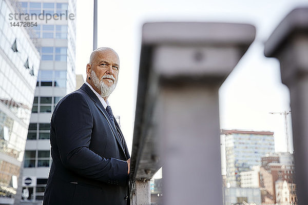 Eleganter Geschäftsmann lehnt in der Stadt am Geländer und schaut auf die Aussicht