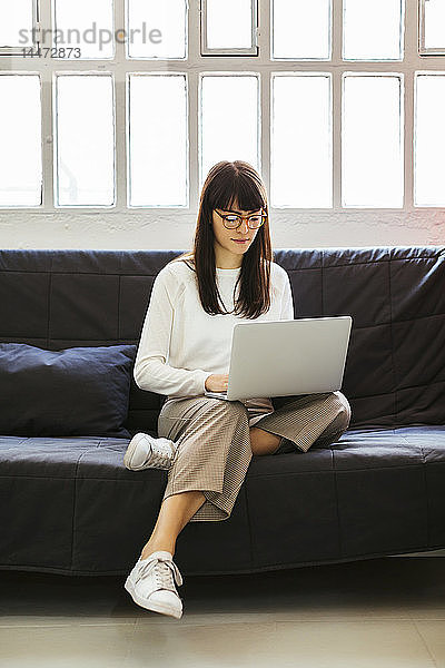 Junge Frau sitzt im Büro mit Laptop auf der Couch